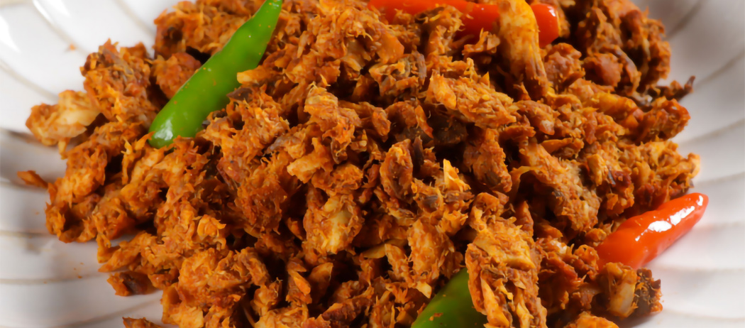 Close-up of spicy fried shredded meat with green and red chili peppers on a white plate.