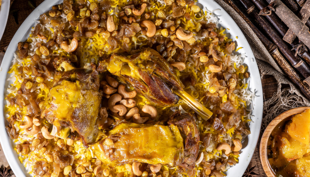 Plate of Majboos Lahm featuring roasted lamb pieces served over saffron rice with nuts and fried onions.